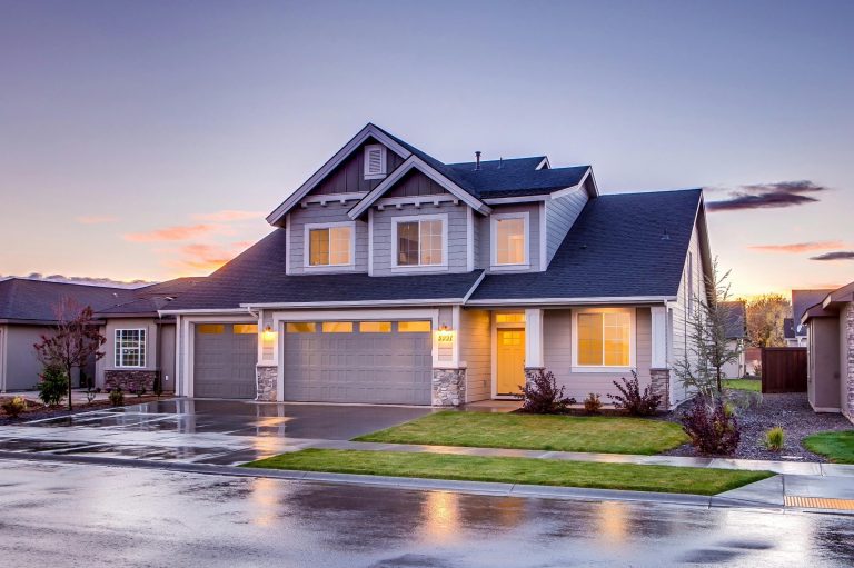 A home with a garage and driveway illuminated by a warm sunset, casting long shadows on the ground.