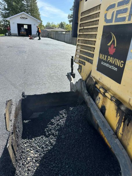 A man operates a paving machine while working on a driveway.