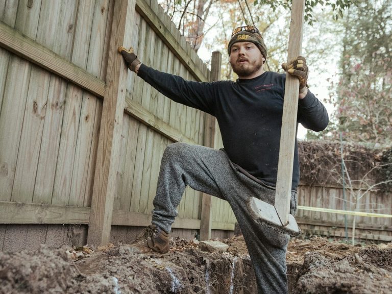 A man holds a wooden fence post in his hands, preparing for installation or repair work.